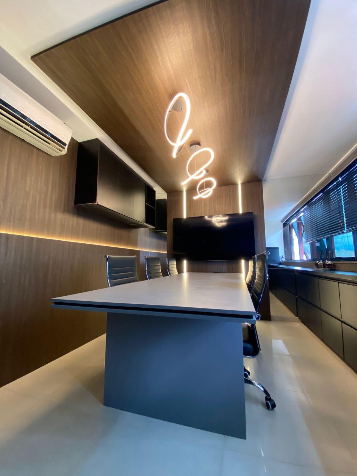Sala de reunião com paredes amadeiradas, mesa grafite e frisos de LED