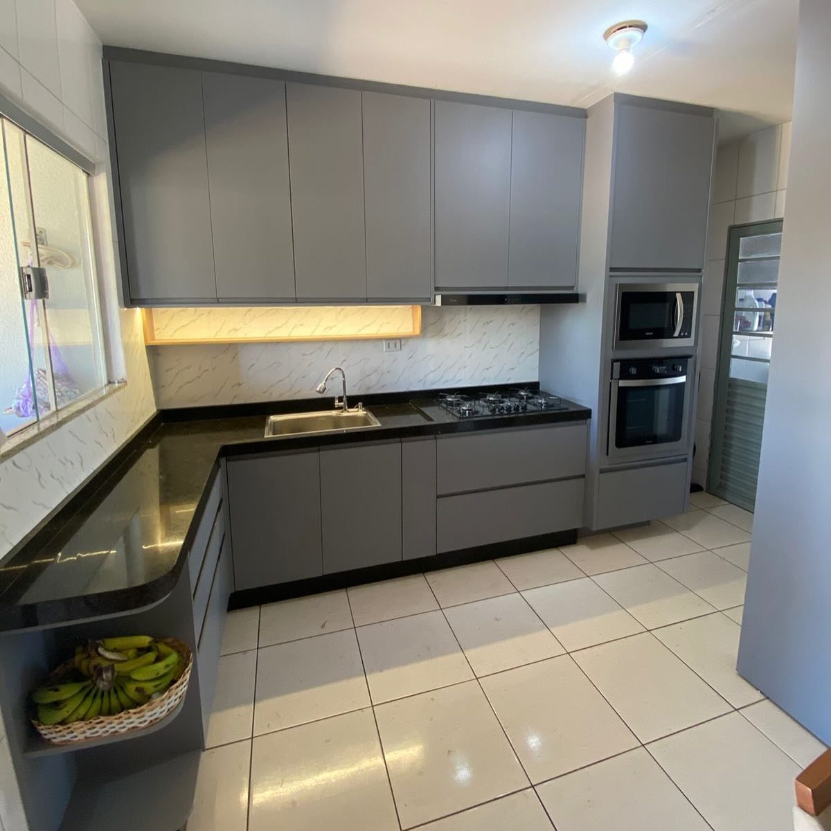 Cozinha cinza em L com torre para forno e micro-ondas e bancada de granito preto